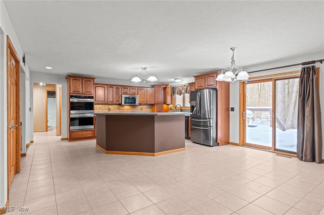 Spacious kitchen with a large island, wood cabinetry, stainless steel appliances, and sliding doors to a snowy yard.