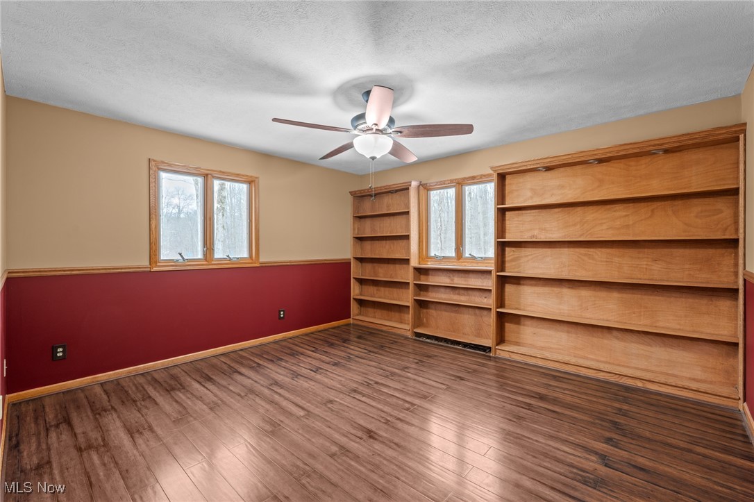 Empty room with built-in wooden bookshelves, two windows, and a ceiling fan.