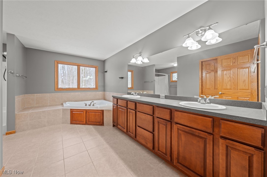 Spacious bathroom with double vanity, soaking tub, and warm wood cabinetry.