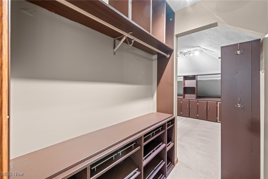 Walk-in closet with dark built-in shelving, drawers, and hanging rods opening to an adjoining dressing area.