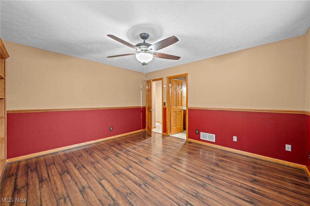Empty room with red lower walls, wood-look flooring, and a ceiling fan.