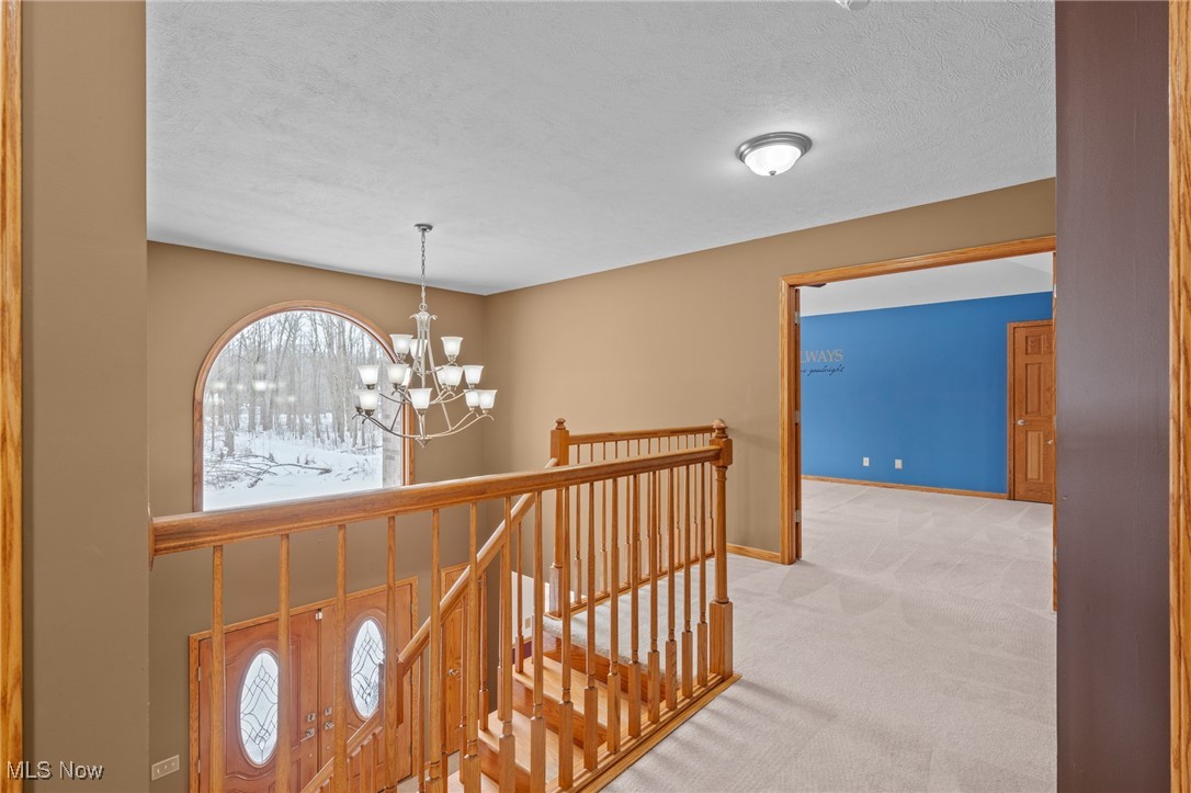 Upstairs landing with a wood staircase railing, chandelier, and arched window overlooking snowy trees.
