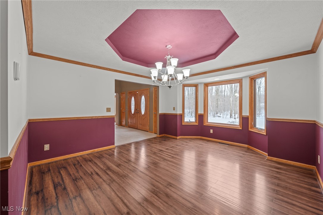 Dining room with burgundy walls, wood floors, a chandelier, and windows overlooking snowy woods.