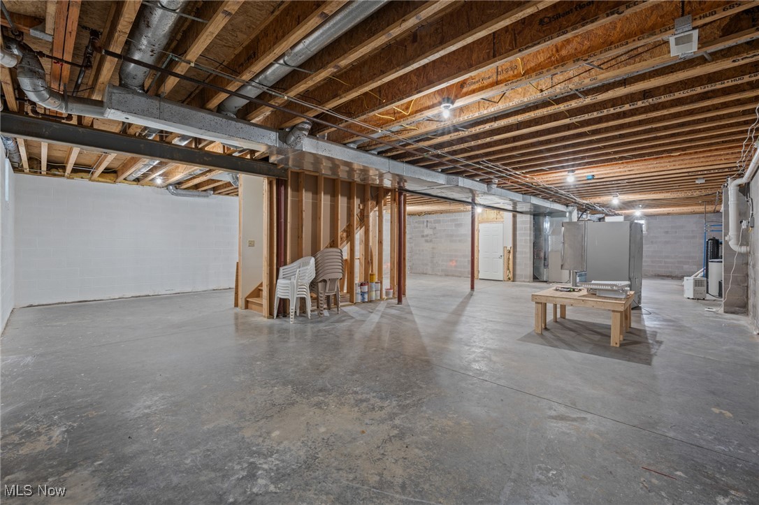 Unfinished basement with exposed joists, concrete floor, partial wall framing, and mechanical equipment.