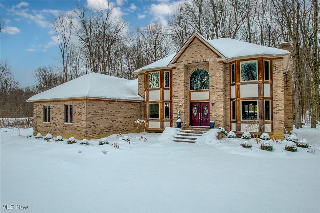 Two-story brick house in snow, with arched window and dark red double front doors.