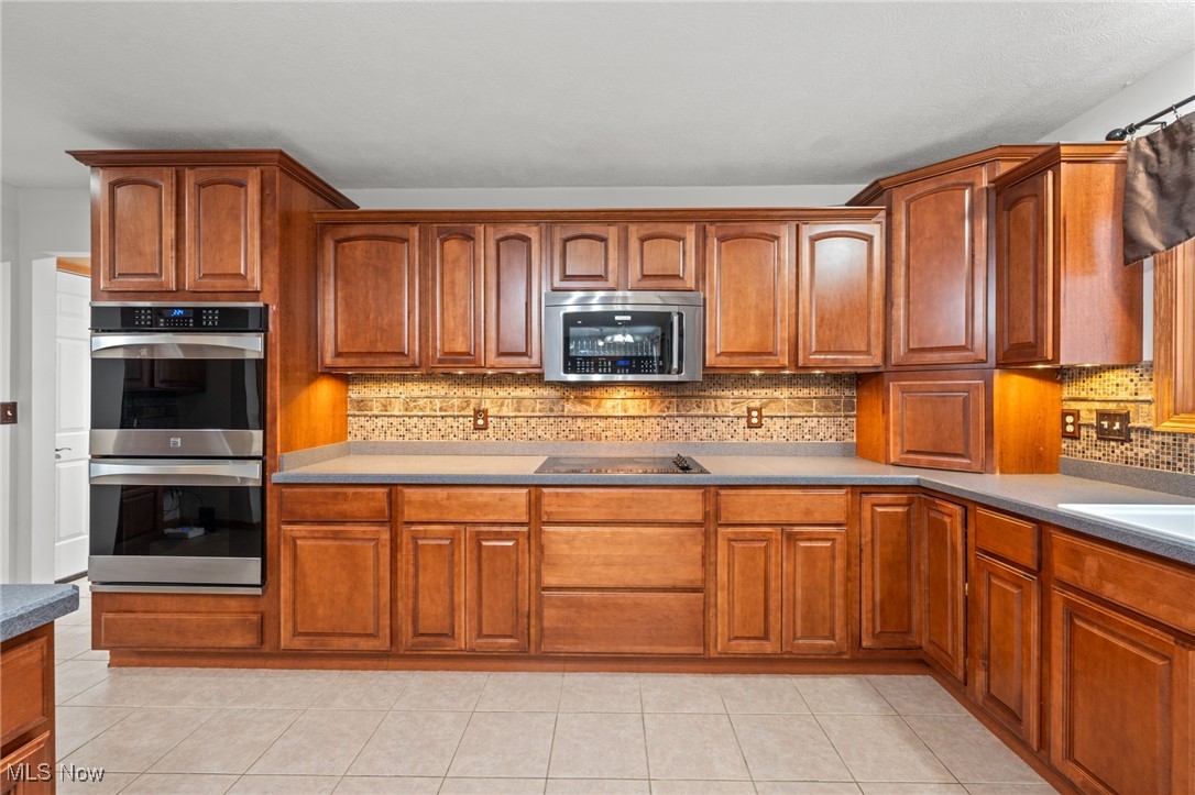 Kitchen with reddish-brown cabinetry, double wall ovens, and a tiled backsplash.