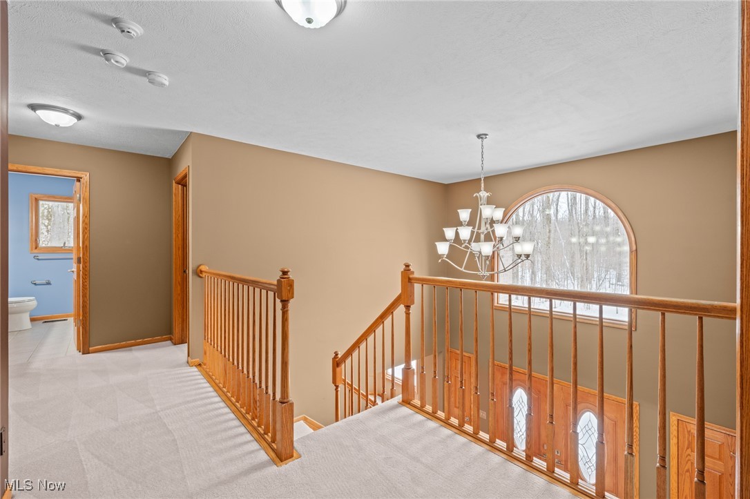 Upstairs landing overlooking a staircase, with wooden railings and a chandelier beneath an arched window.