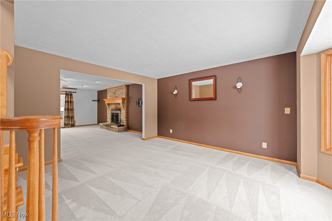 Empty carpeted living room with a brown accent wall and brick fireplace.