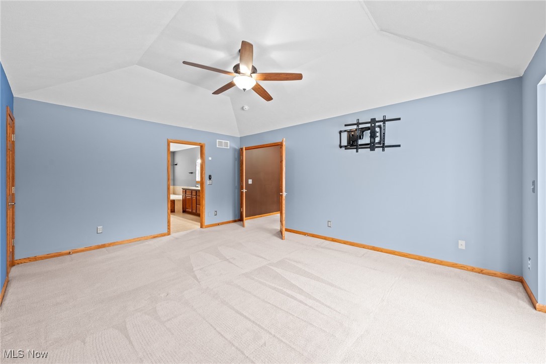 Empty bedroom with blue walls, vaulted ceiling, and a wood-blade ceiling fan.