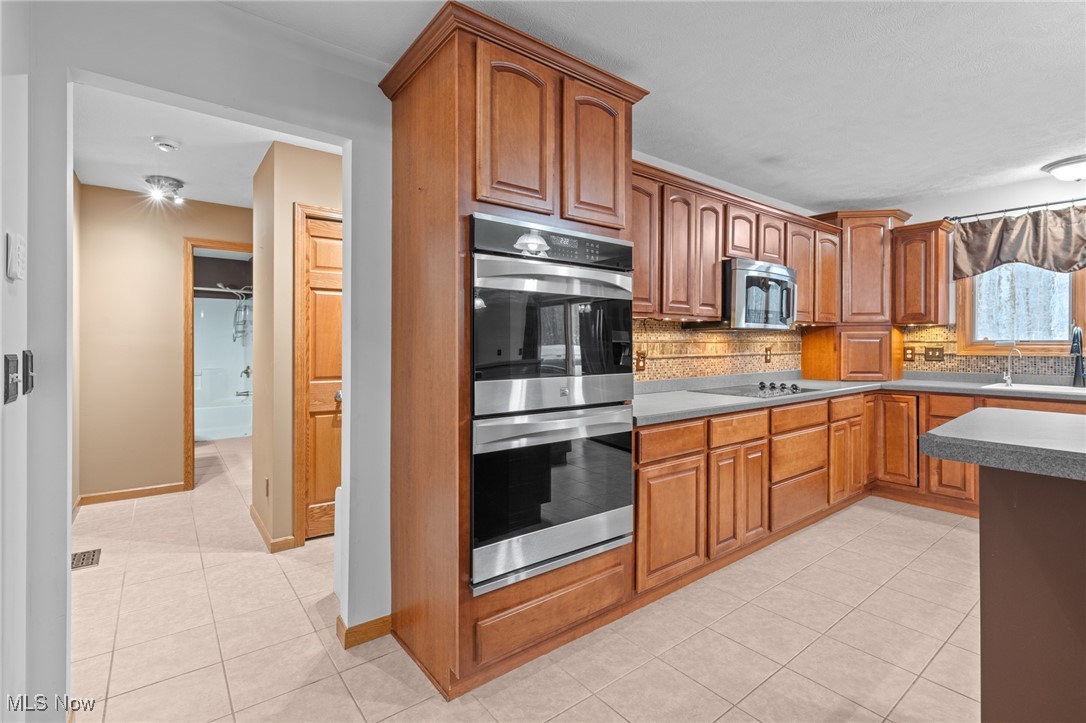 Kitchen with wood cabinets, stainless steel double ovens, tiled backsplash, and a gray-topped island.
