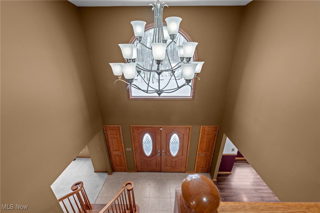 Two-story foyer with a chandelier, arched window, wooden double doors, and stair railings.