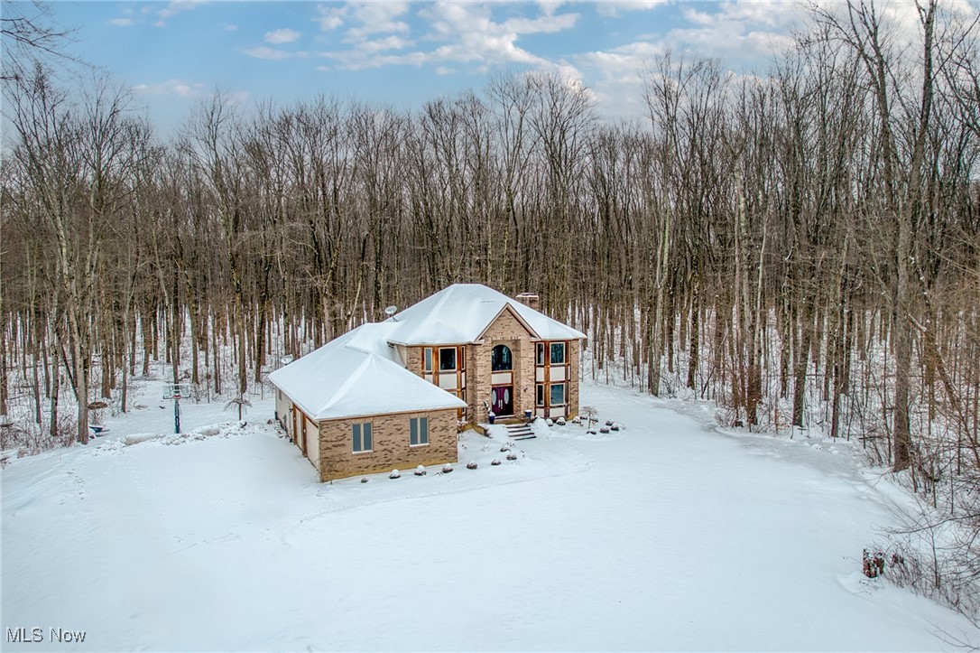 Aerial view of a two-story stone house surrounded by snow-covered yard and leafless woods.