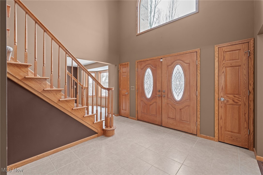 Entry foyer with a wood staircase, tiled floor, and double front doors with oval glass inserts.