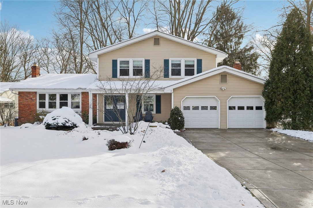 Two-story beige home with a brick wing, double garage, and snow-covered yard.