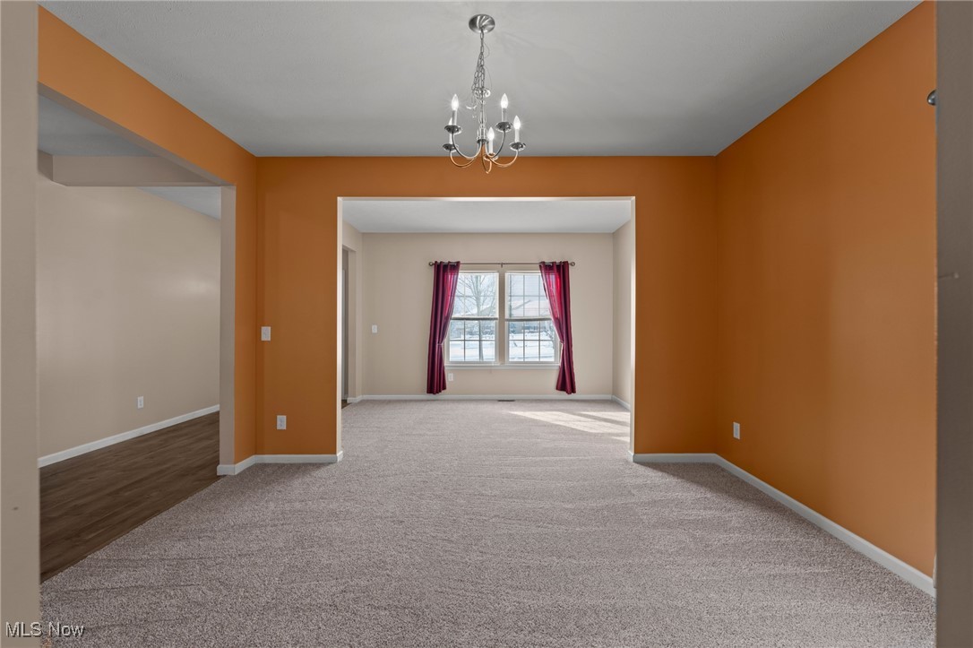 Empty carpeted room with burnt-orange walls and a chandelier, opening to a window with burgundy curtains.