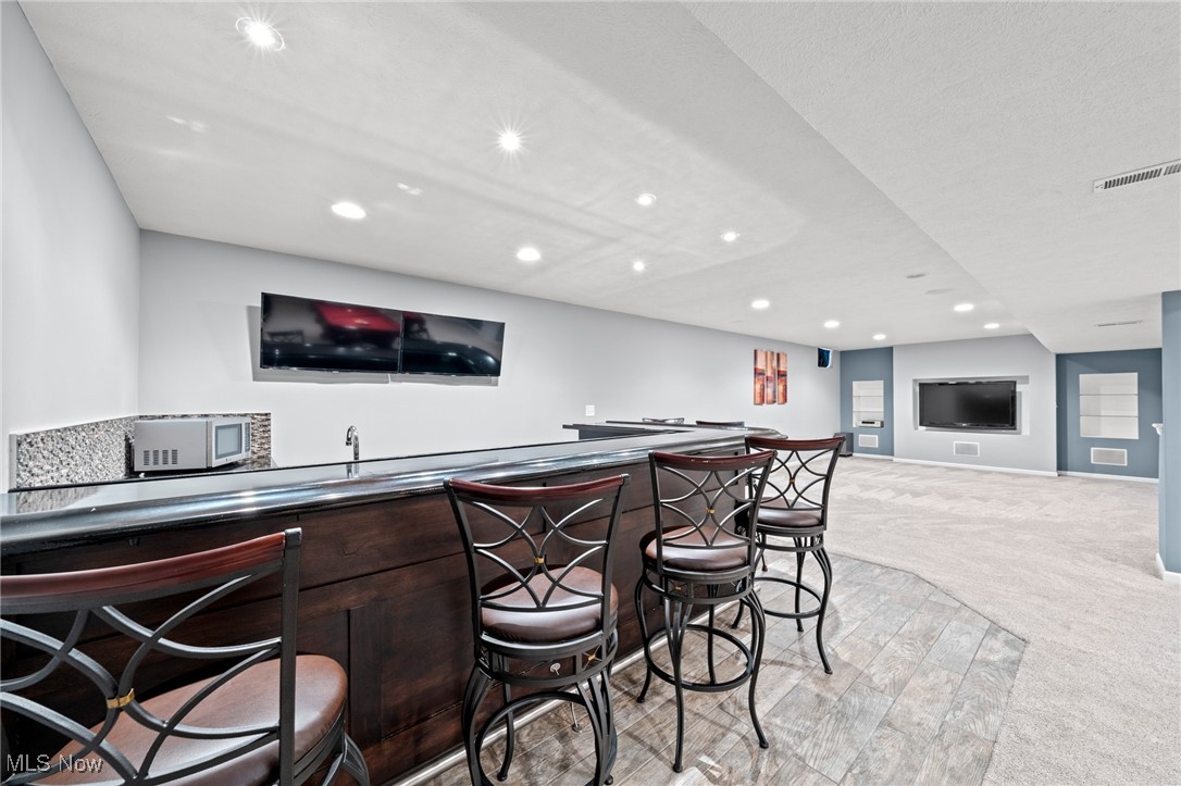Basement recreation room with a long dark-wood bar, metal stools, and televisions.