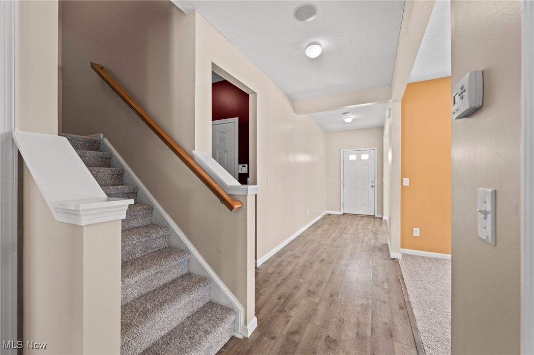 Entry hall with wood-look flooring, a carpeted staircase, and a white front door.