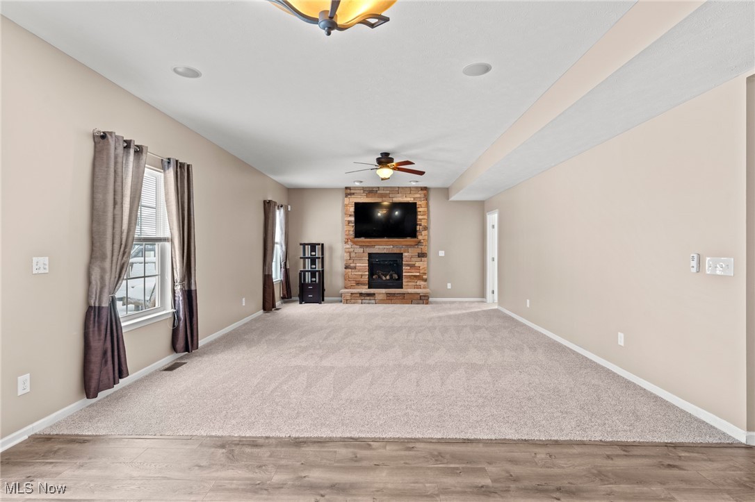 Spacious living room with a stone fireplace, television, curtained window, and carpeted floor.