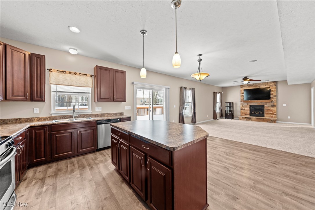 Open kitchen with dark wood cabinets and island adjoining a living area with a stone fireplace.