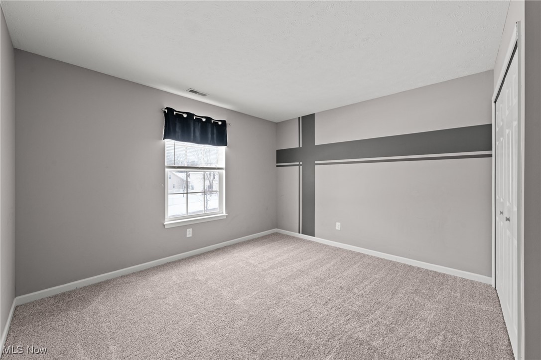 Empty bedroom with beige carpet, a gray geometric accent wall, and a window overlooking snow.