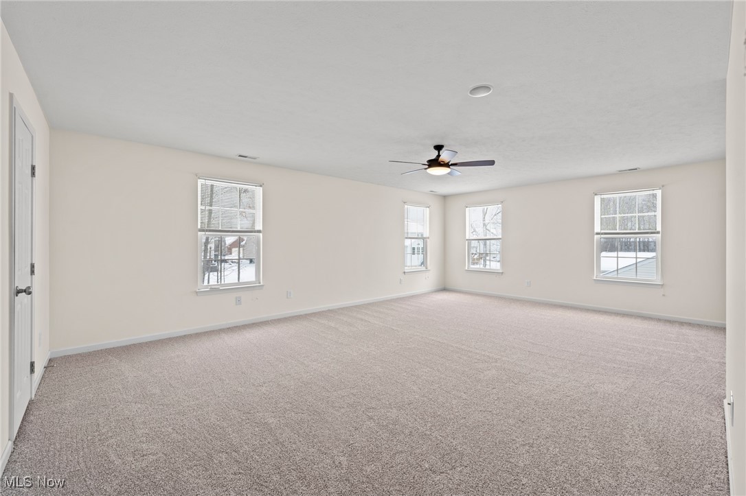 Empty carpeted room with several windows and a ceiling fan.