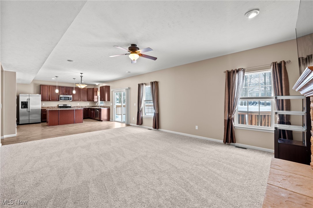 Empty living room opening to a kitchen with dark wood cabinets and a stainless-steel refrigerator.