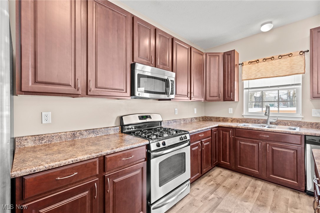 Kitchen with reddish-brown cabinets, stainless steel gas range, and sink beneath a window.
