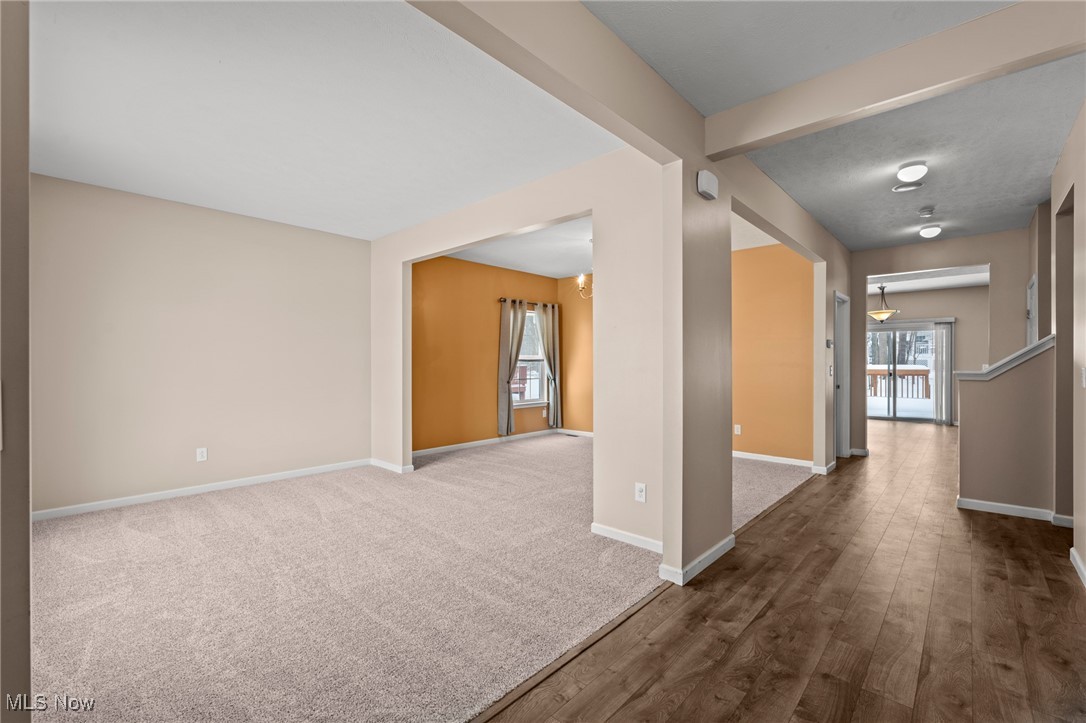 Carpeted living area opens to an orange-accented room and wood-floored hallway.