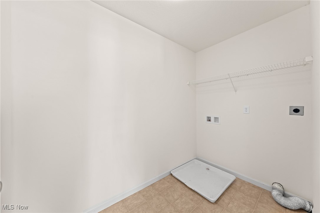 Empty laundry room with a washer drain pan, wall hookups, and a wire shelf.