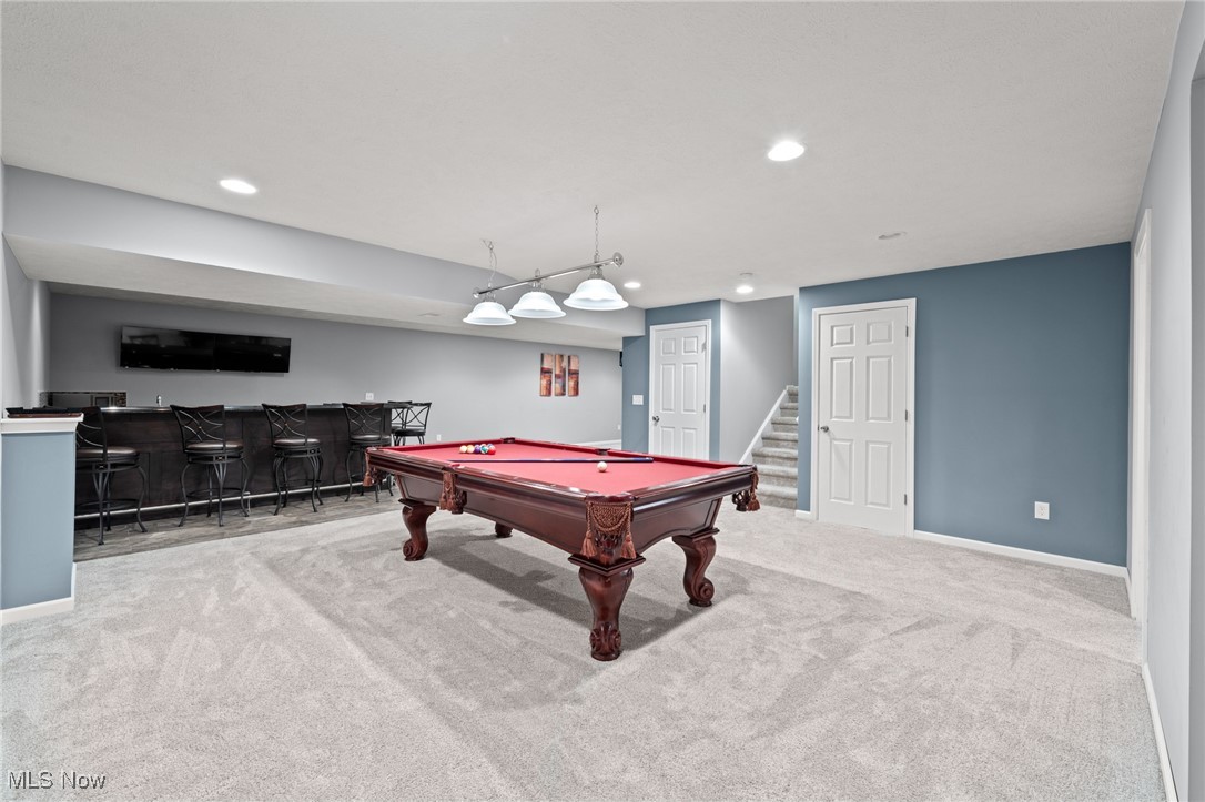Basement game room with a red-felt pool table, long bar, and stairs.