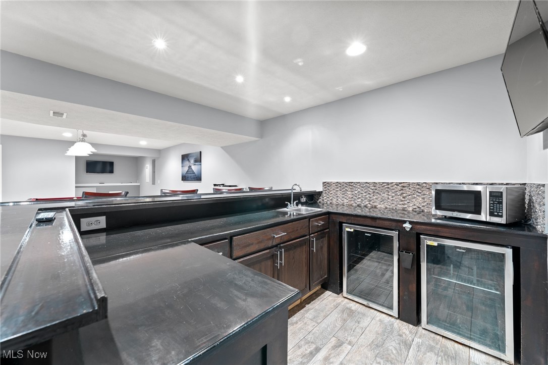 Wet bar with dark stone counters, a sink, microwave, and two beverage refrigerators.