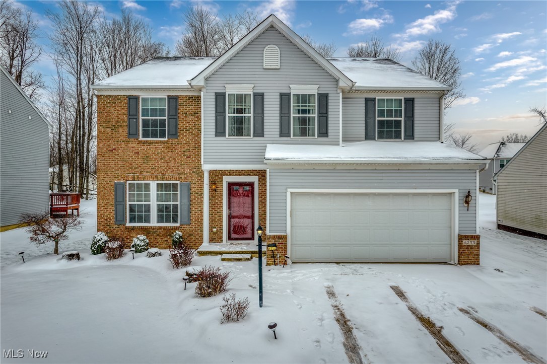 Two-story gray and brick home with a red front door and double garage in a snowy yard.