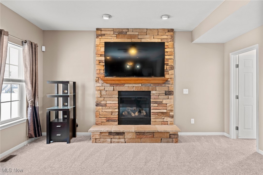 Living room with a tan stone fireplace, mounted television, and curtained window.
