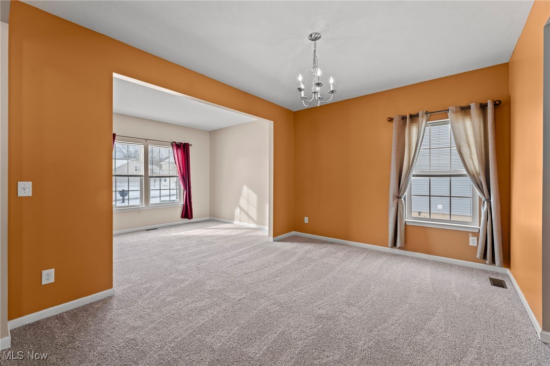 Empty carpeted room with orange walls, a chandelier, and a wide opening to an adjoining room.