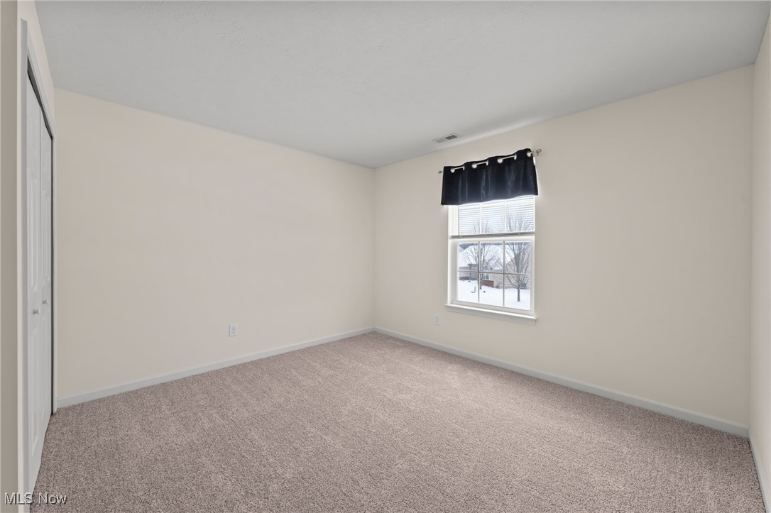 Empty bedroom with taupe carpet, white closet doors, and a window overlooking snow.