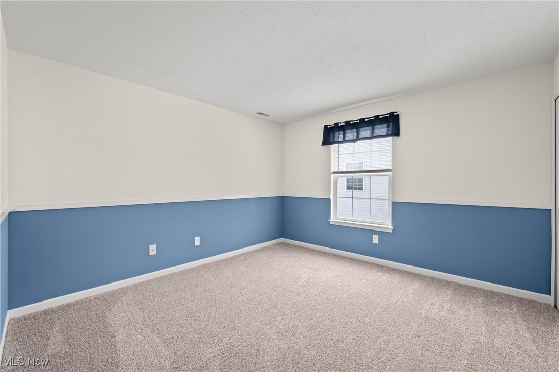 Empty bedroom with blue-and-cream walls, beige carpet, and a window with blinds.