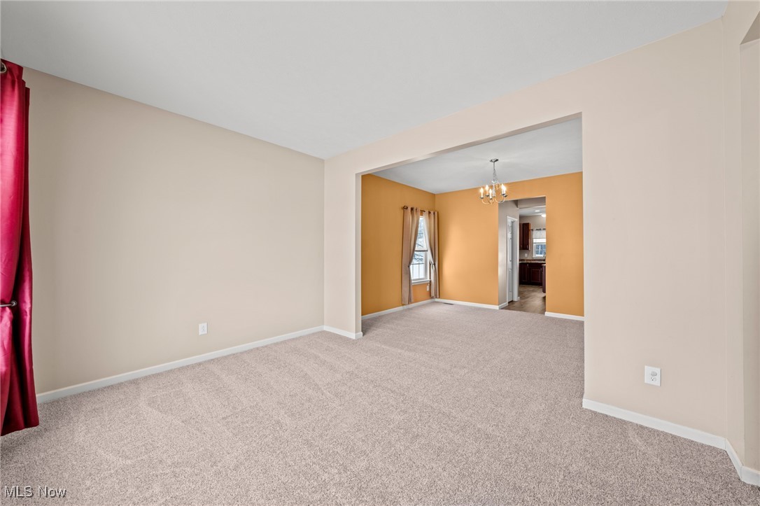 Carpeted living room opening to an orange dining area with a chandelier and kitchen doorway.