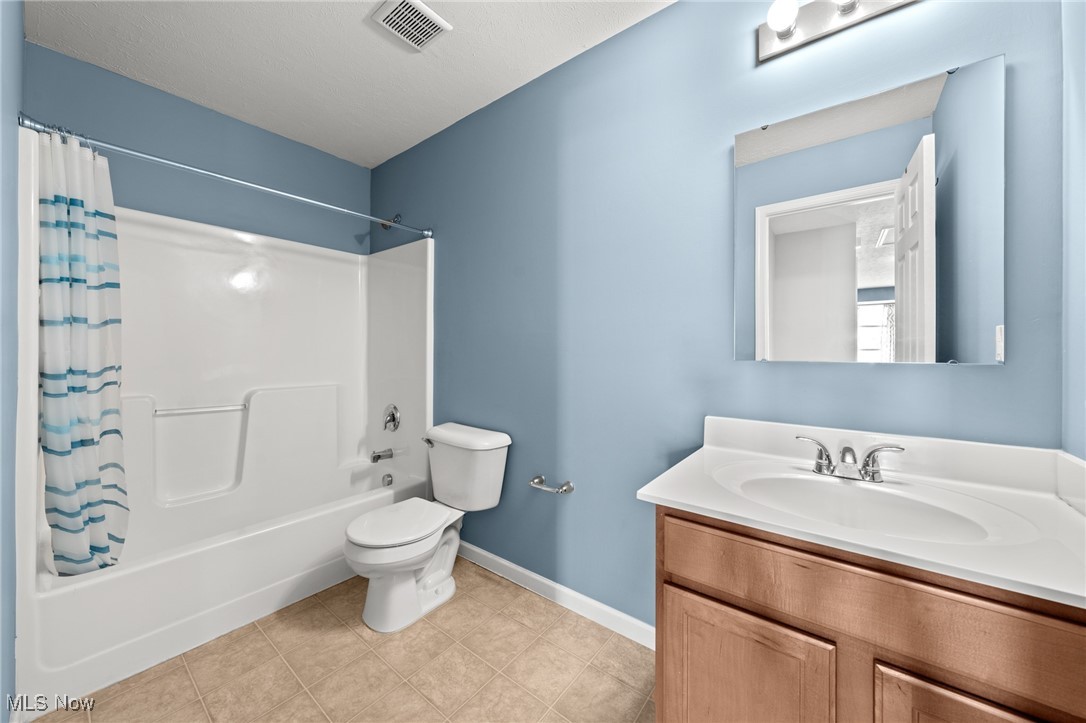 Bathroom with a white tub and shower, blue-striped curtain, and wood vanity.