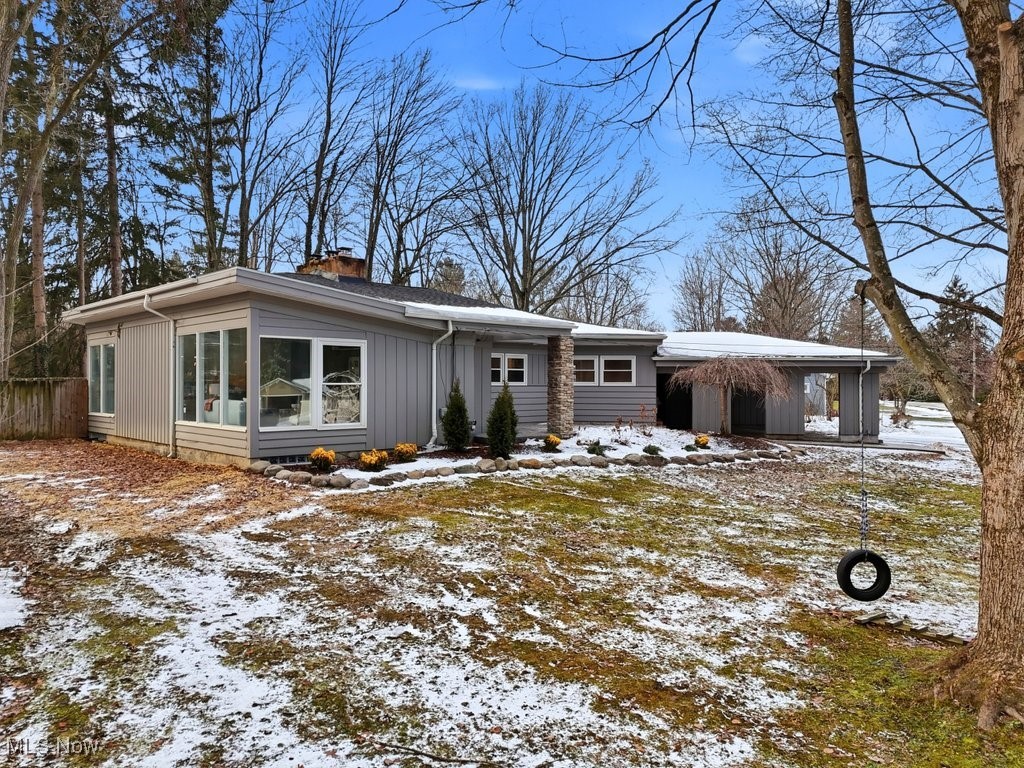 Gray single-story home with broad windows and an attached carport in a patchy-snow yard with a tire swing.