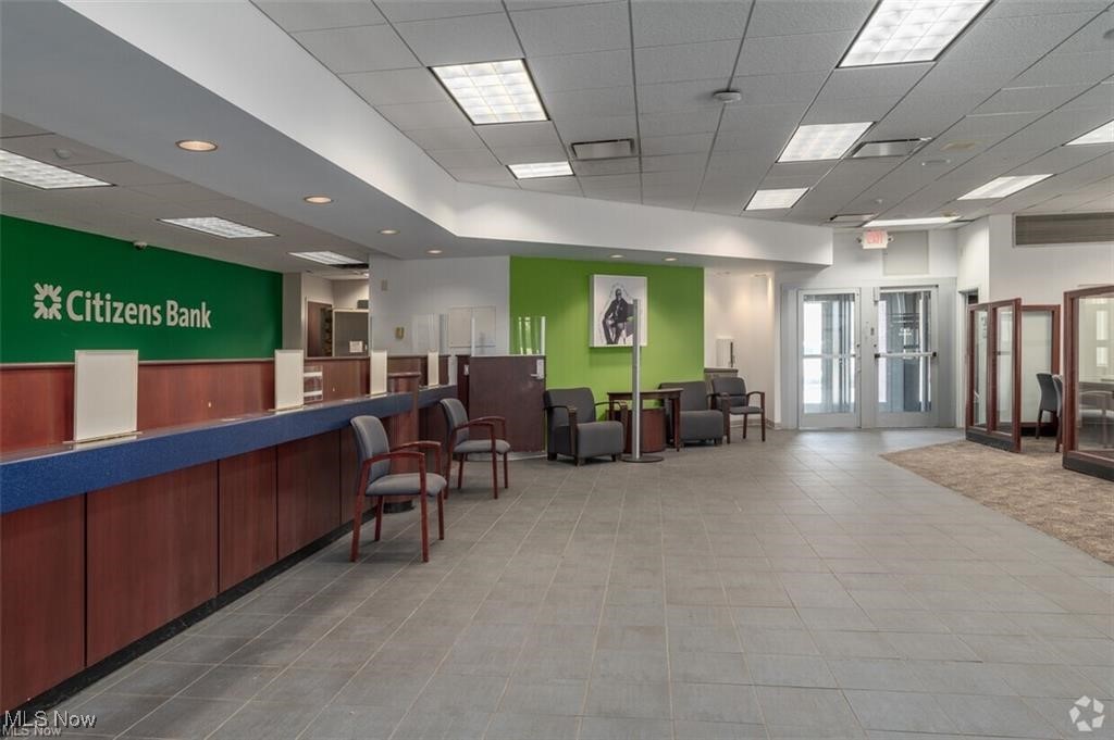 Bank lobby with a long service counter, waiting chairs, green accent wall, and glass entry doors.