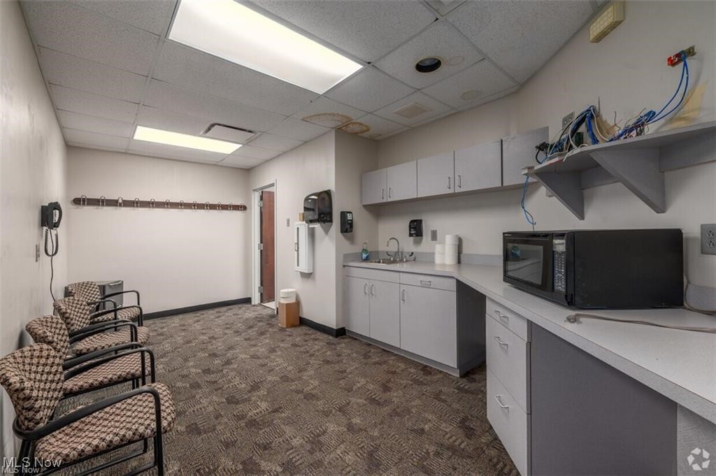 Office waiting area with patterned chairs, built-in cabinets, a counter, sink, and microwave.