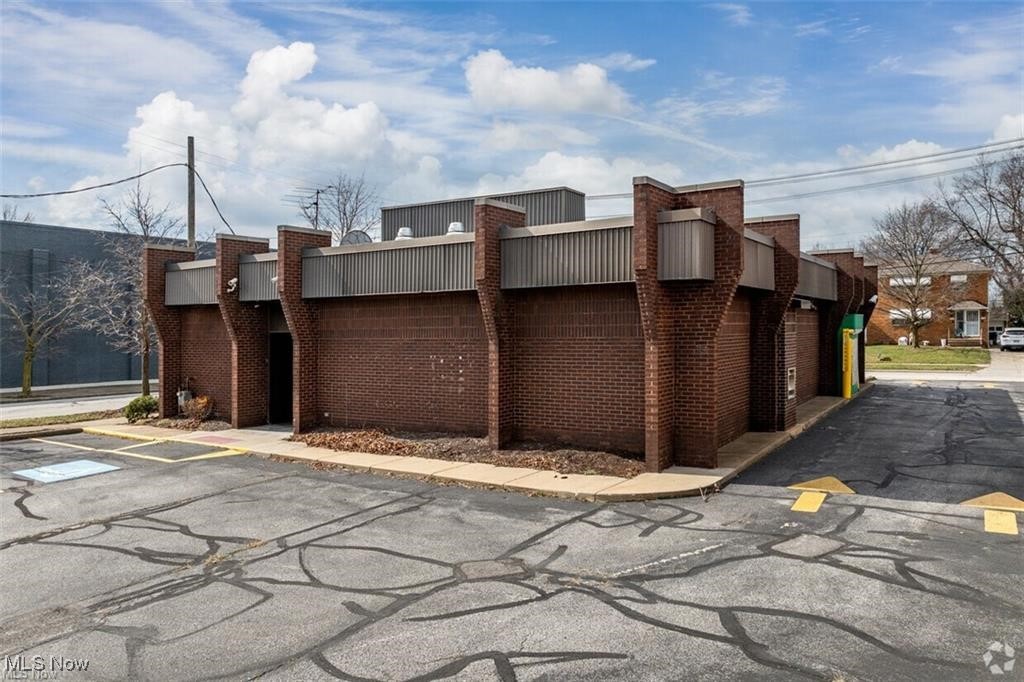 Low brick commercial building with angular facade and paved parking area.
