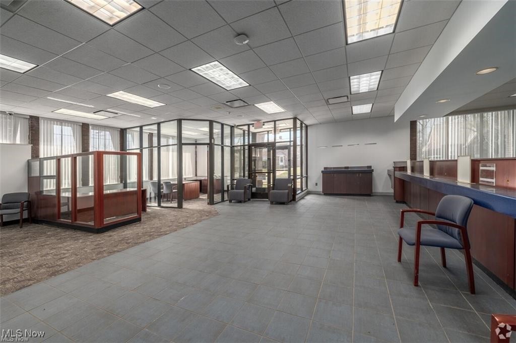 Commercial office interior with glass-partitioned offices, reception counters, and gray tiled floors.