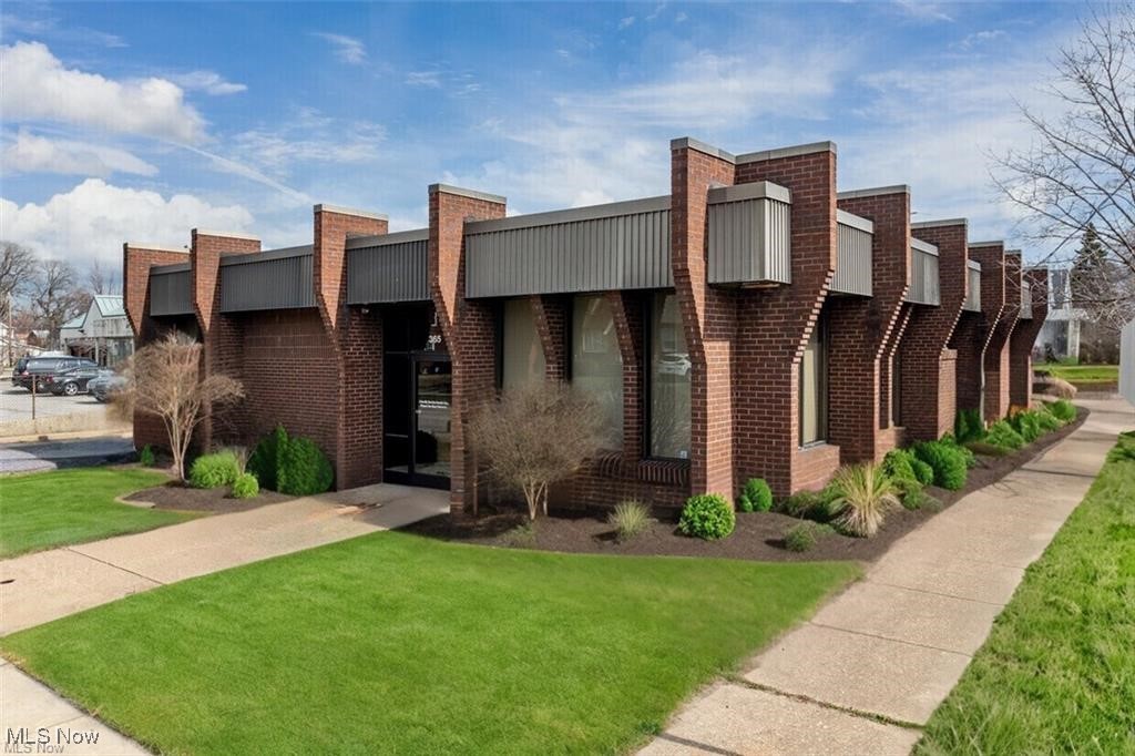 Brick commercial building with gray metal panels, a glass entrance, and landscaped lawn.