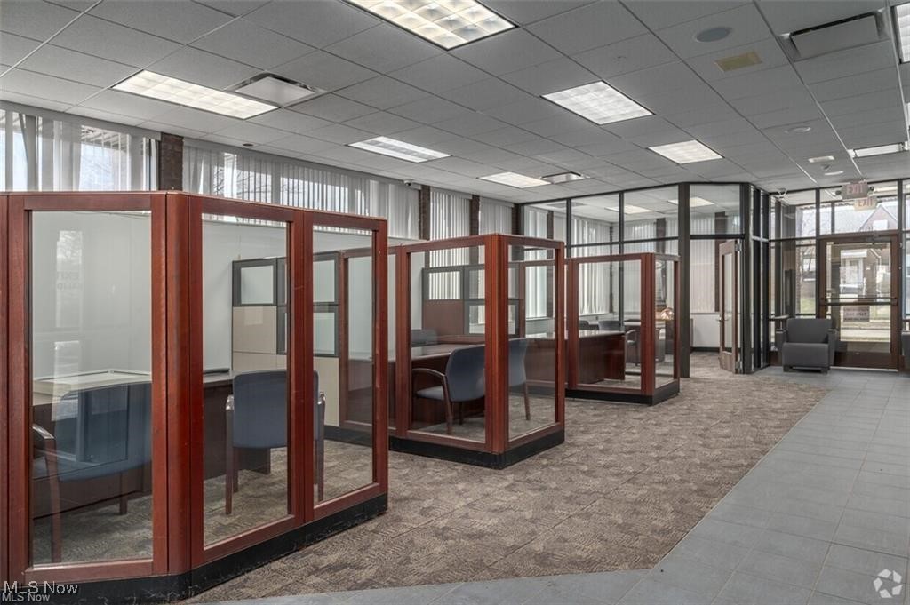 Commercial office interior with glass-partitioned work areas and reddish-brown wood frames.