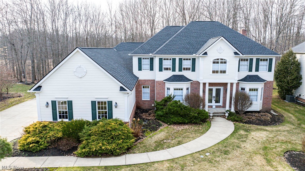 Two-story white house with brick accents, dark shutters, attached garage, and curved front walkway.
