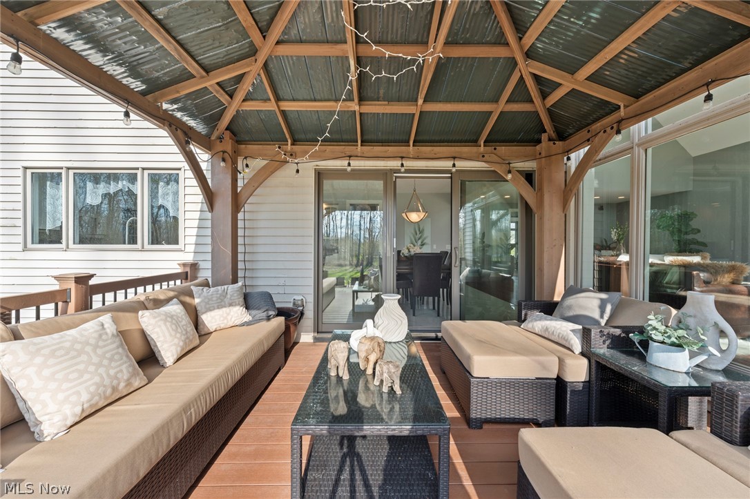Covered patio with timber roof, wood decking, and beige sectional seating beside sliding glass doors.