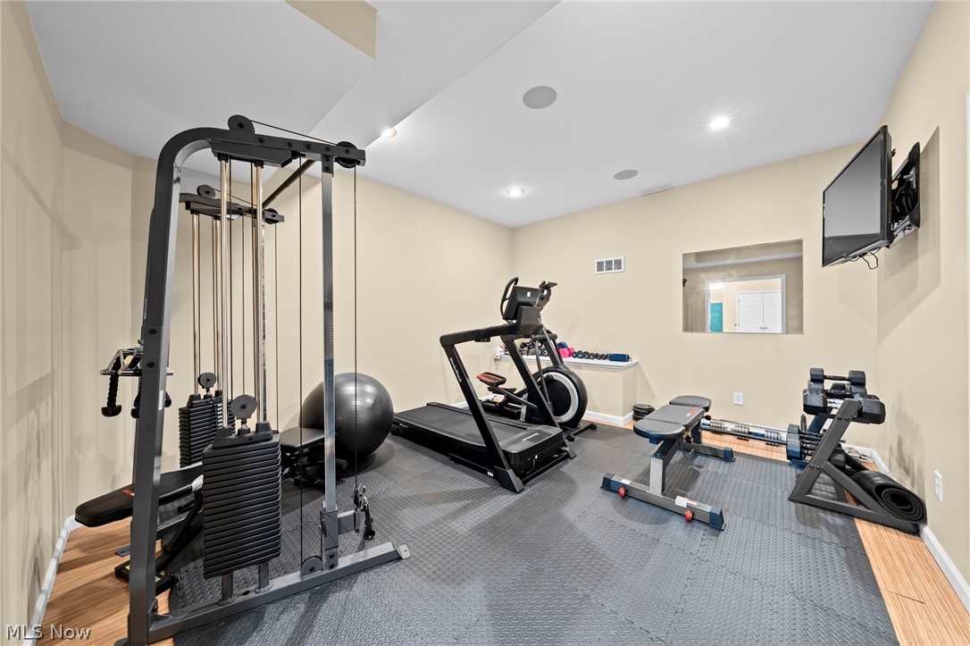 Home gym with a cable machine, treadmill, stationary bike, weights, and wall-mounted TV.