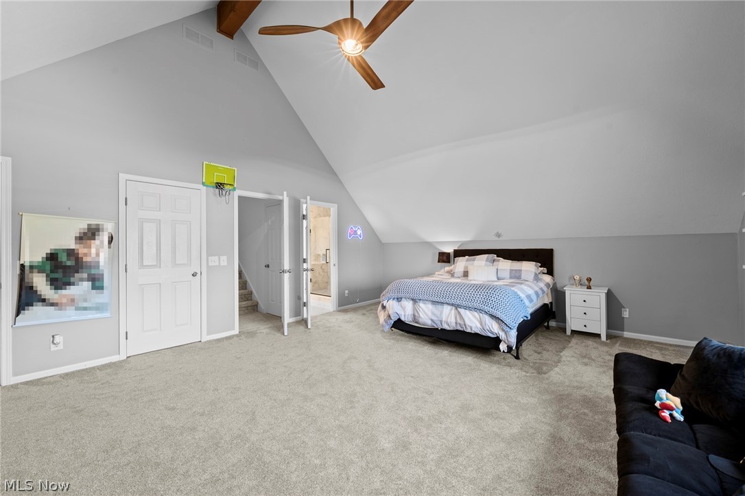 Furnished bedroom with a vaulted ceiling, exposed beams, ceiling fan, and basketball hoop above the door.