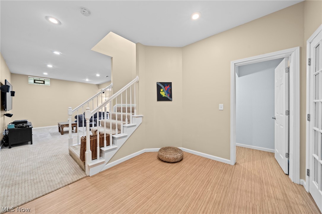 Finished basement recreation area with carpeted stairs, white railing, and adjoining doorway.